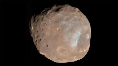 Rappresentazione artistica di una sonda spaziale in orbita attorno alla piccola e irregolare luna marziana Phobos, con il pianeta rosso sullo sfondo.